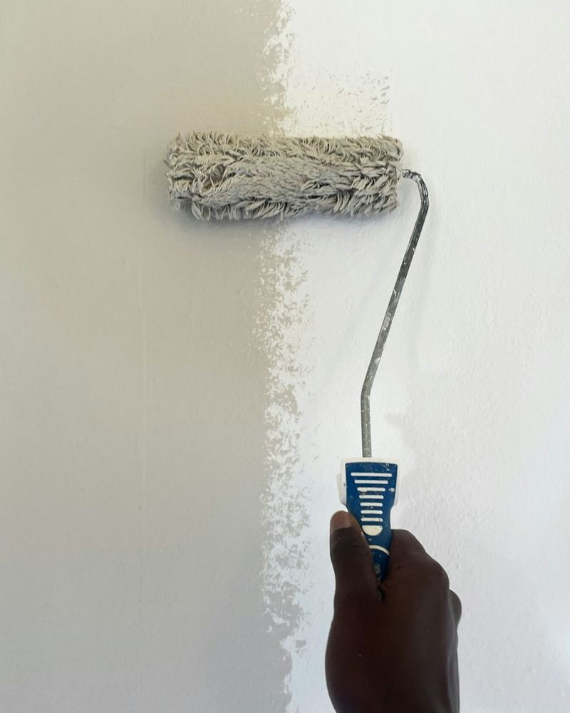 Paint roller covering a wall with a fresh coat of white paint