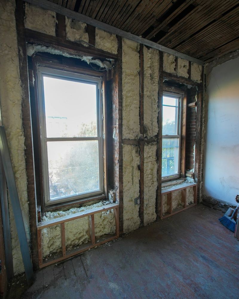 Gutted room mid-renovation with exposed wall framing, insulation and tall windows